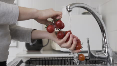 Close-sideways-shot-washing-cherry-tomatoes-with-running-tap-water-at-the-sink-in-the-kitchen