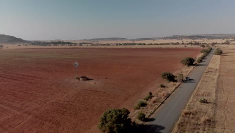 Aerial-fly-over-of-a-working-windpump-in-a-dry-field-with-a-gravel-road
