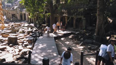 Wide-Exterior-Tilt-Shot-of-Tourists-Walking-down-stairs-and-Across-a-Wooden-Walk-Way-on-Their-Way-to-Explore-an-Ancient-Temple-Near-Angkor-Wat