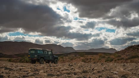Time-lapse-of-cloudscape-over-4WD-vehicle-parked-in-desert,-zoom-out