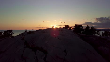 Fly-past-Inukshuk-on-Rocky-Pine-Tree-Island-at-Sunset,-Drone-Aerial-Wide-Dolly-In