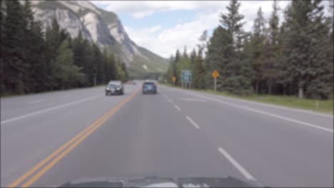 Vista-Panorámica-De-La-Carretera-Local-Que-Conduce-A-La-Ciudad-De-Banff-Desde-El-Interior-Del-Camión-En-Movimiento-Mientras-Corre-Por-El-Bosque-De-Pinos-Con-Un-Cielo-Azul-Claro-En-El-Verano