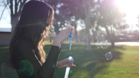 Attractive-young-woman-blowing-dreamy-bubbles-floating-in-the-bright-sunshine-outdoors-with-lens-flare-SLOW-MOTION