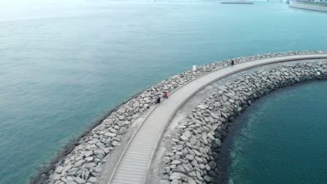 Kreisförmige-Luftaufnahme-Einer-Drohne-Von-Menschen,-Die-Auf-Einer-Steinbrücke-Im-Wasser-Stehen,-Abu-Dhabi,-Vereinigte-Arabische-Emirate