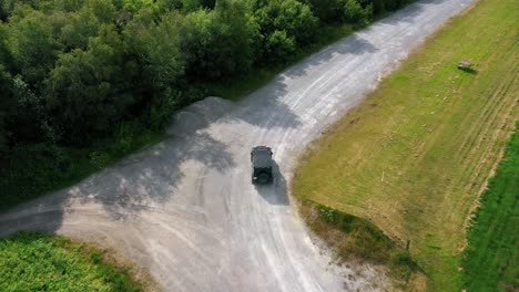 Cinematic-aerial-drone-camera-footage-you-can-see-black-jeep-driving-off-road-in-countryside-landscape-surrounded-by-green-fields