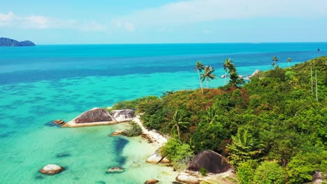 Small-tropical-island-with-palm-trees-secluded-white-sandy-beaches-and-granite-rocks-on-the-shore-washed-by-waves-of-turquoise-crystal-clear-ocean