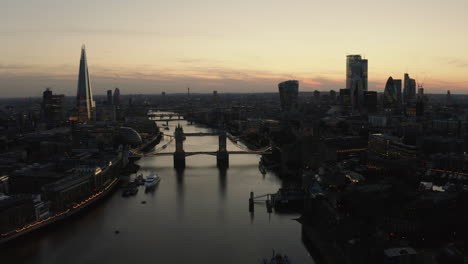 Aerial-view-of-London,-River-Thames-and-Tower-Bridge-just-after-the-sun-has-set-and-the-sky-is-lit