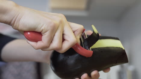 Close-shot-as-peeling-off-the-eggplant-in-the-kitchen,-holding-it-in-hands