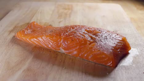 Close-Slow-Motion-Shot-of-Seasoning-a-Fresh-Piece-of-Salmon-Fillet-With-Salt-Prior-to-Cooking-in-the-Kitchen