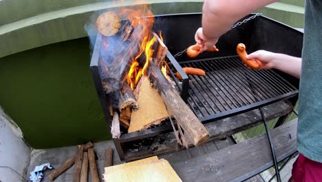 Slow-motion-video-of-a-white-man-putting-sausages-on-a-black-grill-with-burning-fire-on-a-sunny-day