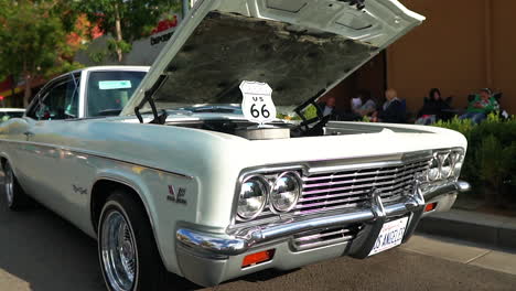 Cream-white-classic-Chevy-Impala-on-display-with-hood-open,-pedestal