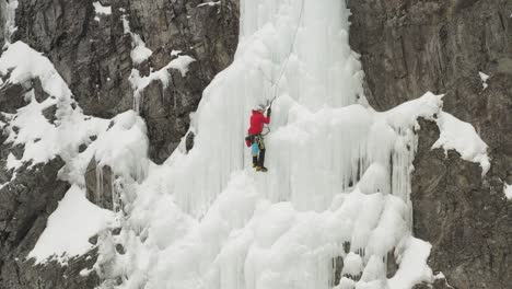 Lone-climber-advances-up-frozen-cascade-spectacular-aerial-4K