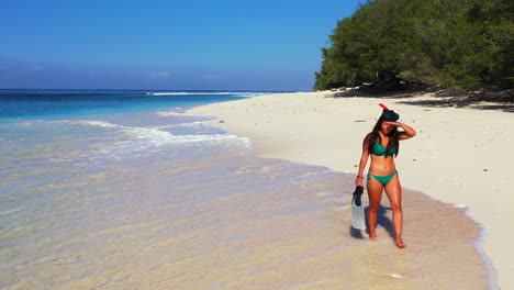 Girls-with-snorkel-mask-and-fins-walking-along-sandy-beach,-searching-for-ideal-place-to-dive-into-blue-sea,-Bali