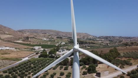 Wind-turbine-turning-in-wind-on-Mediterranean-hilltop,-aerial-closeup-pull-away