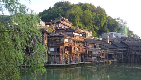 Morning-view-of-the-old-historic-wooden-Diaojiao-houses-on-the-riverbanks-of-Tuo-river,-flowing-through-the-centre-of-Fenghuang-Old-Town