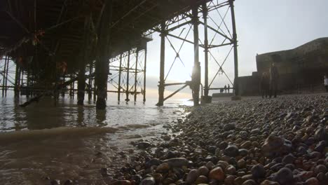 Seagulls-flying-past-beautiful-pebble-beach-coastline-from-under-Brighton-Pier,-in-Sussex,-Uk