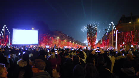 Major-fireworks-and-celebrations-during-the-arrival-new-year-on-Paris's-main-Champs-Élysées,-surrounded-by-a-crowd-of-people-on-main-street-overlooking-the-Triumphal-Arch-and-the-red-covered-street