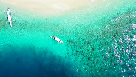 Boats-floating-over-calm-clear-water-of-turquoise-water-seashore-with-coral-reefs-and-rocks-on-sea-bottom-close-to-coast-of-tropical-island-in-Malaysia