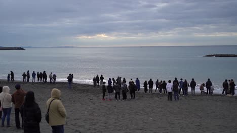 People-enjoying-the-beautiful-waves-of-a-beach-in-Tokyo,-Japan-while-waiting-for-the-sun-to-rise-over-the-horizon---Time-lapse