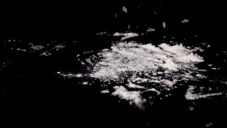 A-person-sprinkling-the-flour-over-table-for-making-a-dough,-isolated-on-black-background