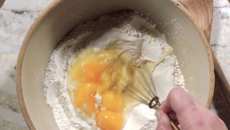 overhead-view-of-whisking-eggs-into-flour-in-large-mixing-bowl