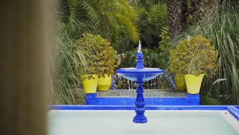 Blue-fountain-in-oasis-garden-of-luxury-mansion,-frame-blocking,-sideways-pan