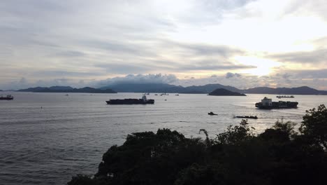 Seeverkehr-In-Der-Bucht-Von-Hongkong-Bei-Sonnenuntergang-Mit-Einem-Großen-Containerschiff,-Das-Vom-Hafen-Wegfährt