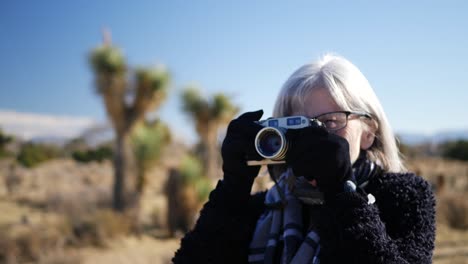 Una-Fotógrafa-Adulta-Tomando-Fotos-Con-Su-Cámara-De-Película-Antigua-Y-Su-Lente-En-Un-Paisaje-De-Vida-Salvaje-Del-Desierto-De-Cerca