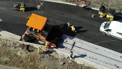 Aerial-view-of-workmen-resurfacing-a-road-with-a-tarmacking-machine