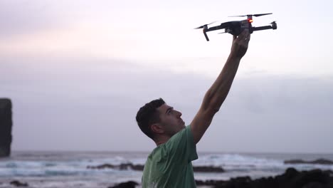 Man-stands-on-coast,-raises-his-arm-and-catches-modern-drone-with-right-hand