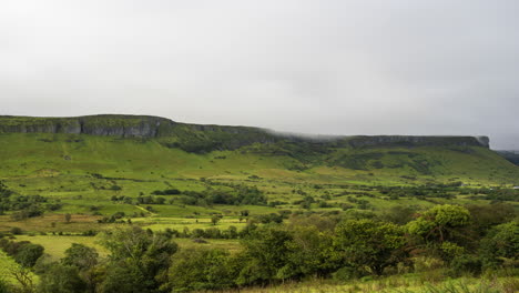 Zeitraffer-Des-Morgennebels,-Der-über-Die-Grünen-Hügel-Oben-Und-Die-Baumlandschaft-Im-Vordergrund-In-Der-Ländlichen-Landschaft-Irlands-Rollt