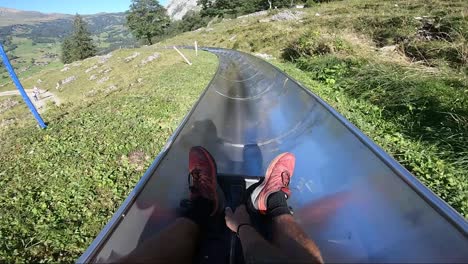 POV-shot-of-a-man-holding-onto-a-small-toboggan,-sliding-down-a-long-metal-slide-through-the-beautiful-scenery-of-the-Swiss-alps