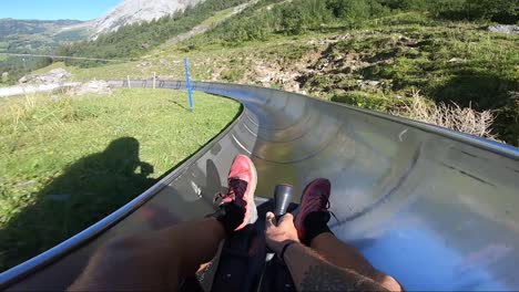POV-shot-of-a-man-holding-onto-a-small-toboggan,-sliding-down-a-long-metal-slide-through-the-beautiful-scenery-of-the-Swiss-alps