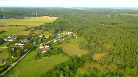 Aerial---flying-over-private-houses-surrounded-with-green-leafy-forest-in-Sasino-village,-Poland-on-sunset