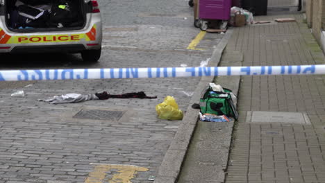 A-discarded-paramedic-kit-lies-next-to-strewn-clothing-at-the-scene-of-a-stabbing-in-a-cobbled-street-behind-police-cordon-tape