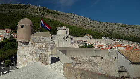 Toma-De-La-Bandera-Croata-Ondeando-En-La-Pared-En-El-Casco-Antiguo-De-Dubrovnik-Con-Mt-Srd-En-El-Fondo