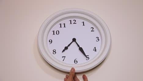 Hand-adjusting-or-repositioning-a-clock-on-the-wall,-close-up