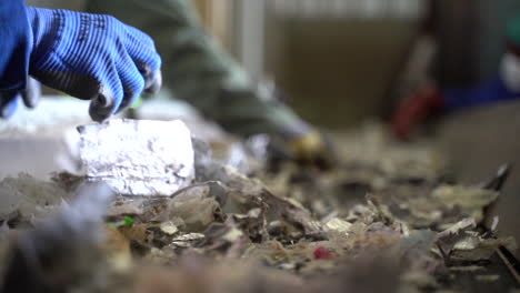 cinematic-shot-of-men-wearing-gloves-sorted-shredded-milk-cartons-on-conveyor-belt-in-recycling-factory