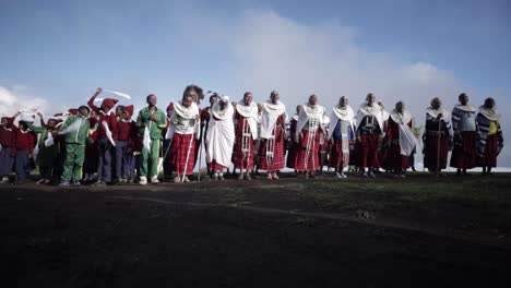 Eine-Gruppe-Von-Dorfbewohnern-Und-Schulkindern-Des-Maasai-Massai-Stammes-Tanzen-Und-Springen-Für-Eine-Kulturelle-Traditionelle-Zeremonie-In-Ihrer-Traditionellen-Kleidung-In-Tansania,-Afrika-–-Zeitlupen-Flachaufnahme
