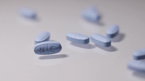 Blue-pills-being-thrown-onto-a-white-reflective-surface-in-slow-motion