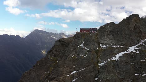 Aerial-shot-flying-over-the-Dossen-hut-with-the-Swiss-flag-next-to-the-steep-cliff-going-down-to-the-valley-of-the-alps-in-the-mountain-region