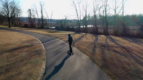 An-aerial-tracking-of-a-man-on-an-electric-skateboard-in-an-empty-park-on-a-sunny-day