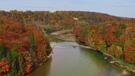 Slow-pullback-aerial-shot-of-an-river-flowing-through-colorful-orange,-red-and-green-idyllic-parts-of-a-forest