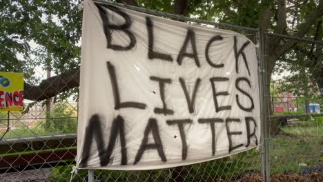 A-sheet-with-the-words-BLACK-LIVES-MATTER-spray-painted-in-black-and-hung-on-a-chain-link-fence
