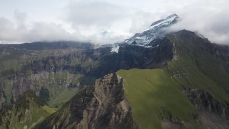 Tiro-Aéreo-Descendente-Sobre-Morgenberghorn-En-Suiza-Avanzando-Hacia-El-Borde-De-La-Cresta-De-La-Montaña-Y-Su-Lado-Rocoso-Y-De-Hierba-En-Contraste-Entre-Sí
