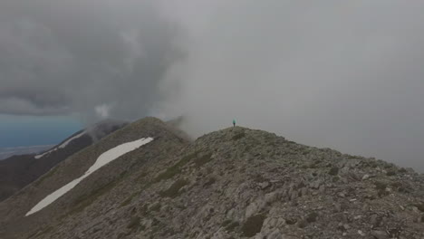Aerial-view-of-a-hike-woman-and-man-that-walk-on-a-mountain-peak-during-a-foggy-day