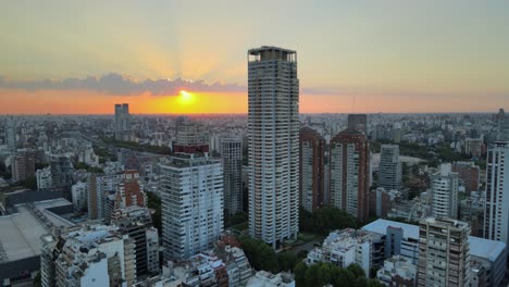 Dolly-in-flying-over-Palermo-neighborhood-buildings-and-skyscraper-at-sunset-with-bright-sun-hiding-behind-clouds,-Buenos-Aires,-Argentina