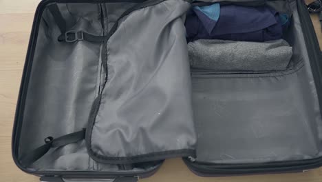 Close-up-shot-of-male-person-packing-small-suitcase,-Carefully-Put-Dresses-Into