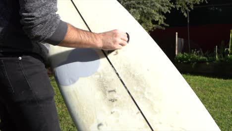 Surfer-removing-wax-from-board-in-home-garden