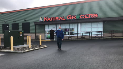Man-In-Mask-Walking-Out-Of-Natural-Grocers-In-Coos-Bay,-Oregon,-wide-shot